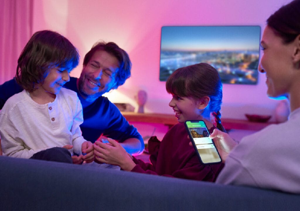 Happy family in living room with woman holding phone open to app for Home Automation Systems